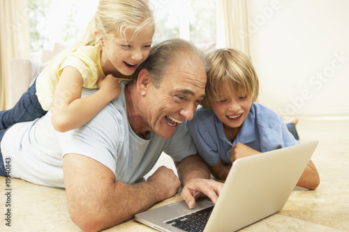 Grandfather AndGrandchildren Using Laptop At Home