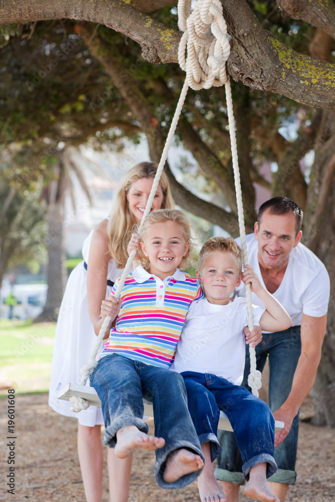 Happy parents pushing their children on a swing Happy parents pushing their children on a swing
