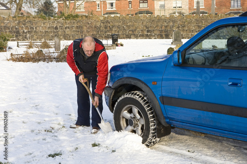 Man clearing snow from around car wheels