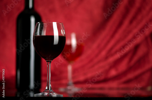 The big glass of red wine and bottle on a red background