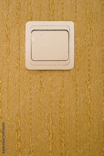 Light switch on a wall with wallpaper of gold color