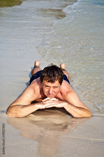 Man in bathingsuit is lying at the beach and enjoying the water