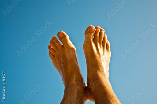 leg and feet of a man in front of the clear blue sky