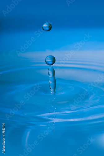Clean blue drop of water splashing in clear water. Abstract blue