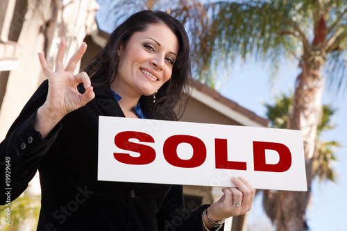 Attractive Hispanic Woman Holding Sold Sign In Front of House