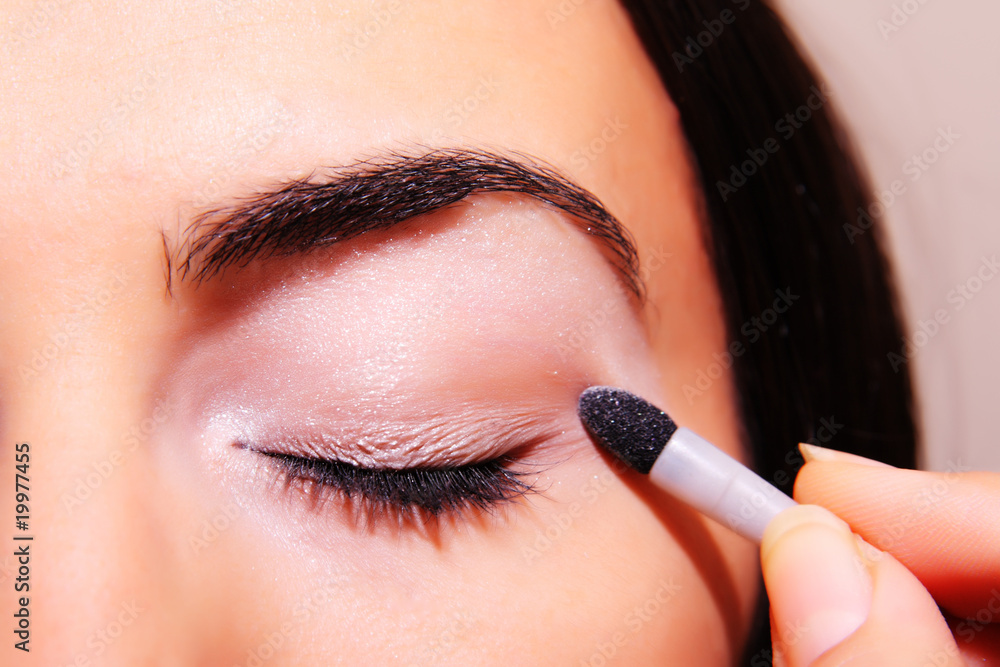 Young woman applying makeup on eye with a cosmetic black pencil