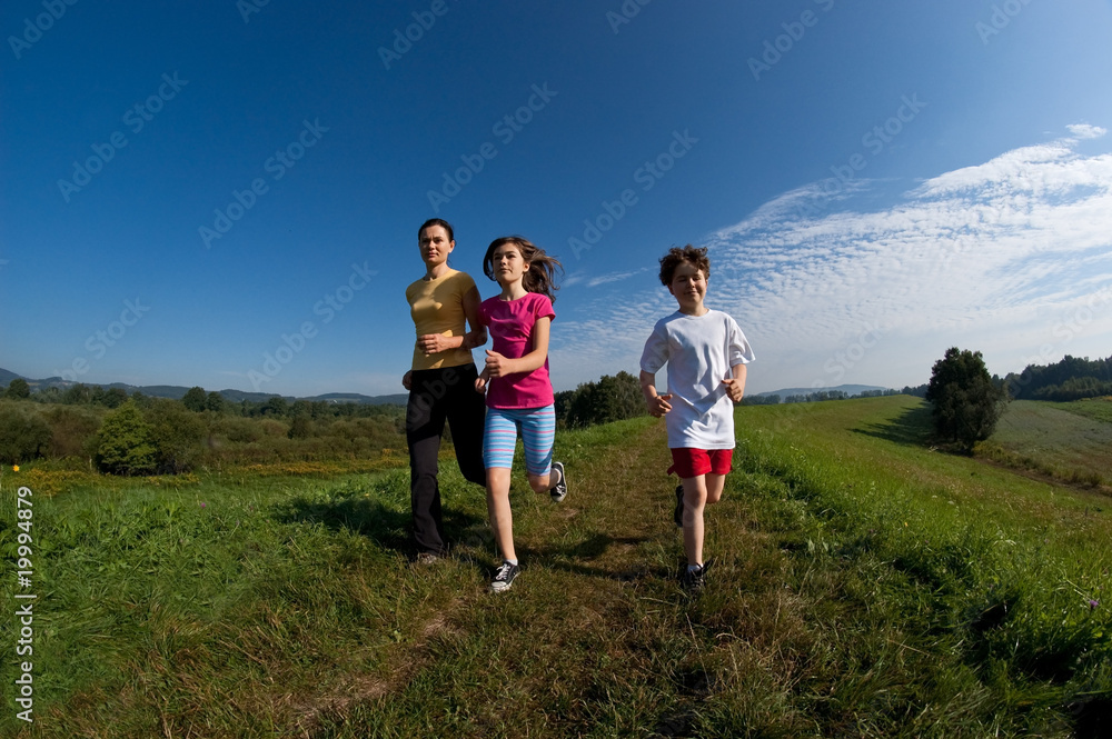 Active family - mother and kids running on green meadow