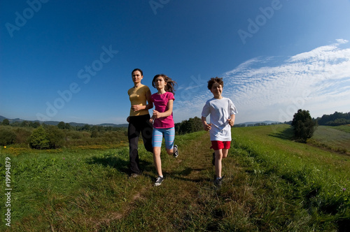 Active family - mother and kids running on green meadow