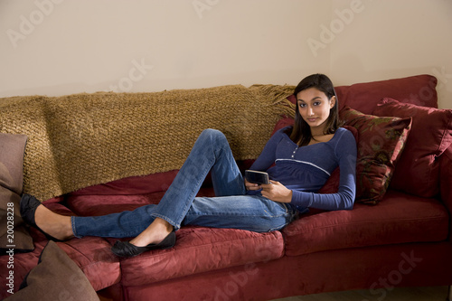 Pretty teenage girl relaxing on sofa texting on mobile phone