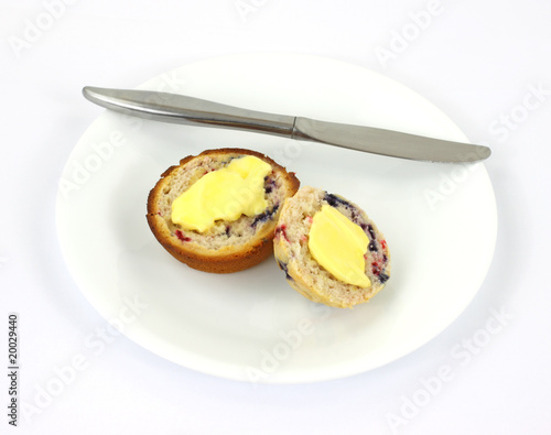 Buttered berry muffin on plate with knife