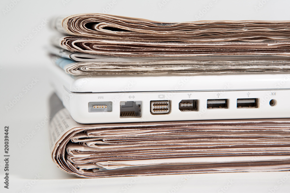 Stapel Zeitungen mit Laptop dazwischen Stapel Zeitungen mit Laptop dazwischen