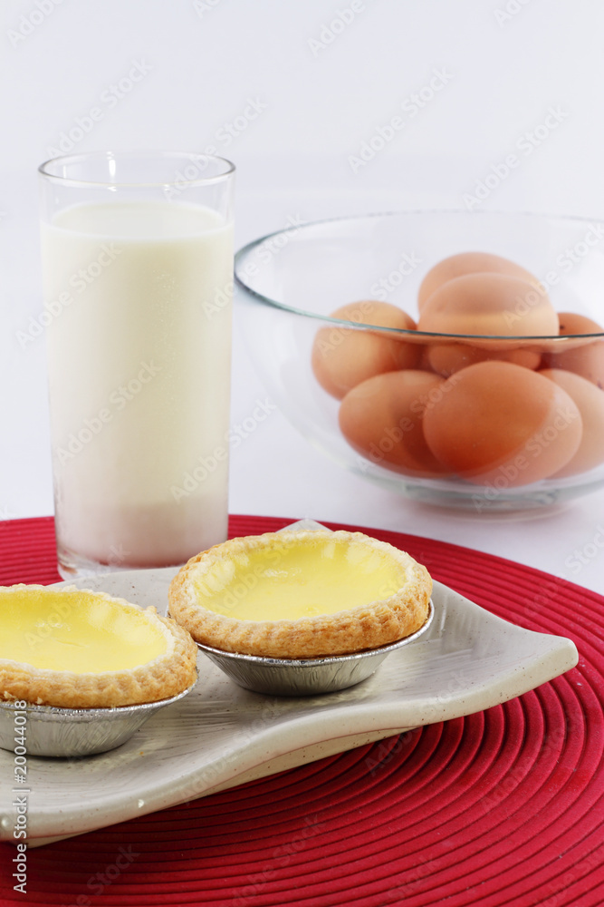 Two egg tarts, milk and a bowl of eggs on a white background Two egg tarts, milk and a bowl of eggs on a white background