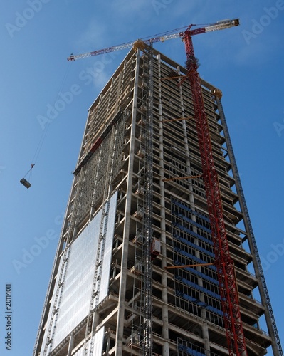 Lifting crane hoisting weight at skyscraper construction site photo