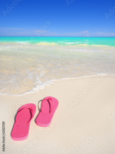 A pair of pink sandals on a white sand beach