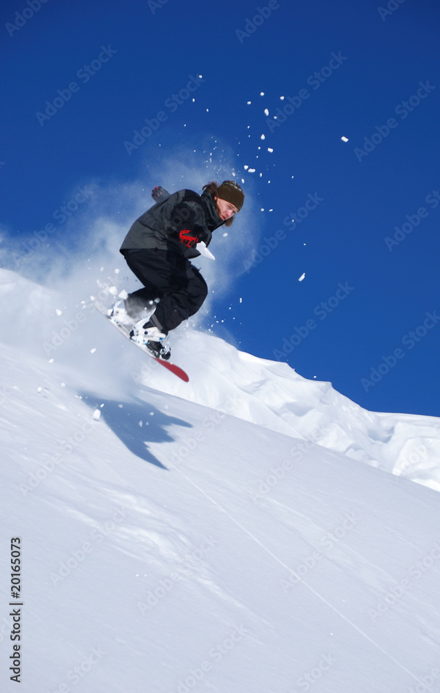 Young snowboarder jumping from snow cornice and splashing snow