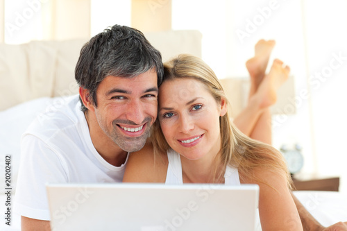 Enamoured couple using a laptop lying on bed