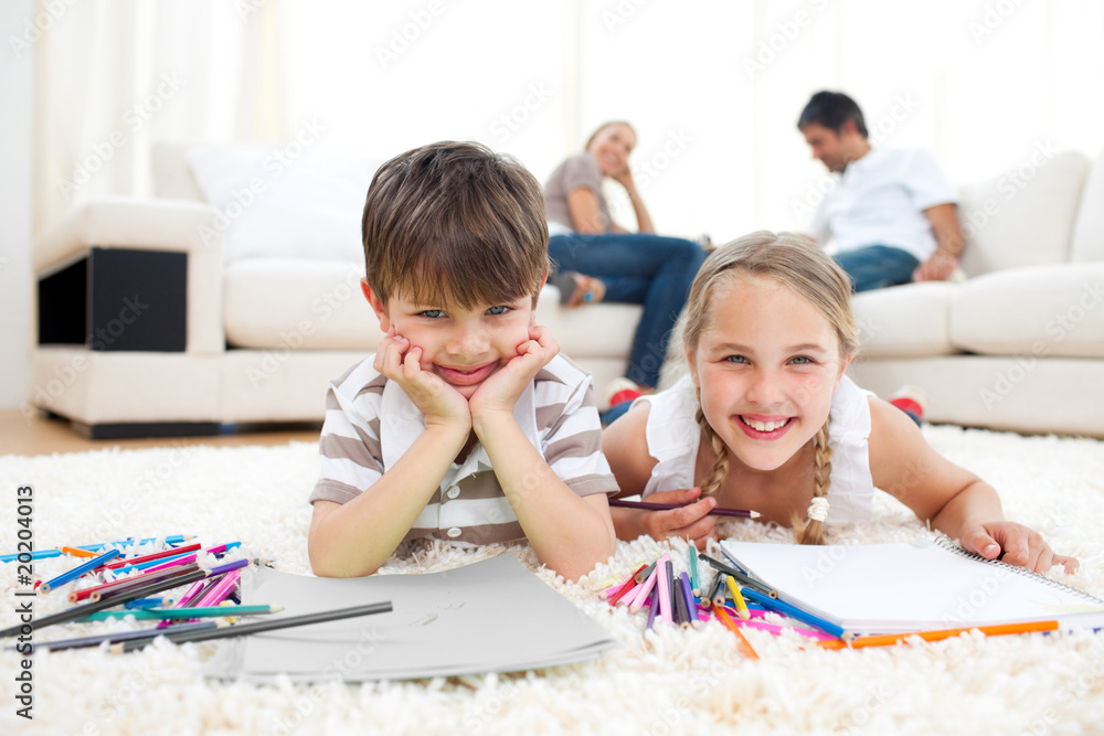 Smiling siblings drawing lying on the floor