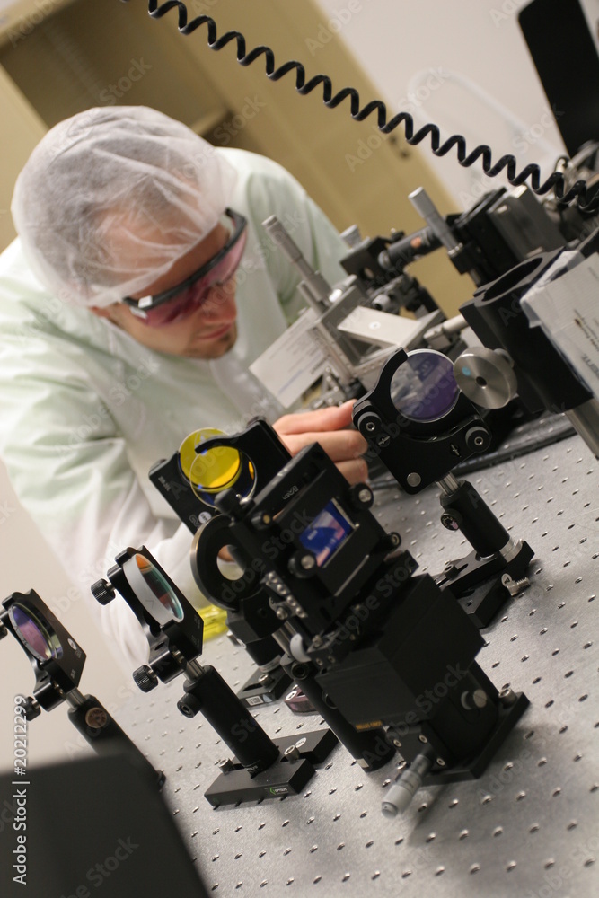 Scientist in a laser laboratory, while researching an preparing a experiment, wearing protection glasses and bonnet Scientist in a laser laboratory, while researching an preparing a experiment, wearing protection glasses and bonnet
