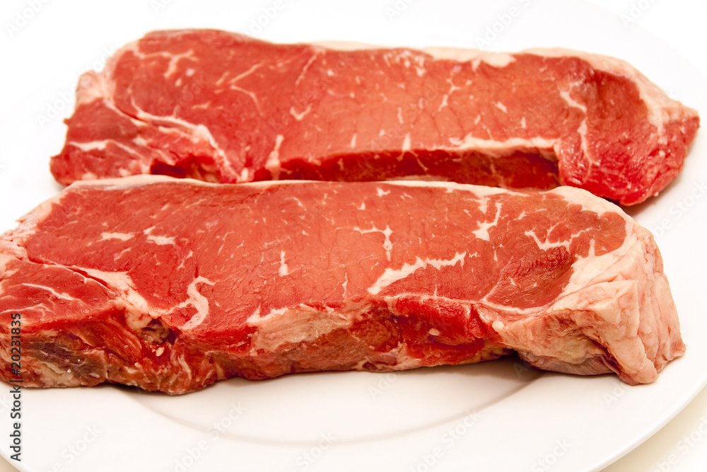 Two Large Strip Steaks on White Plate Two Large Strip Steaks on White Plate