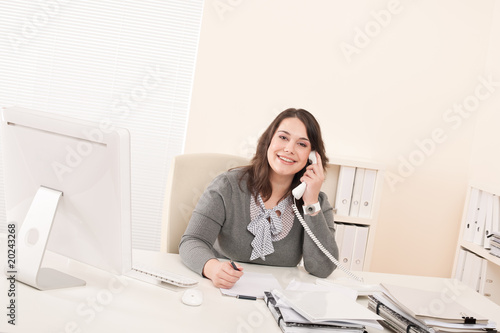 Smiling young business woman on phone at office