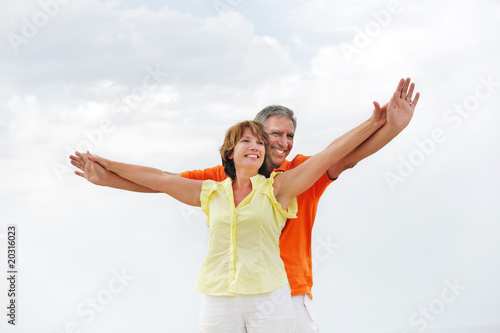 Happy mature couple standing with arms outstretched.