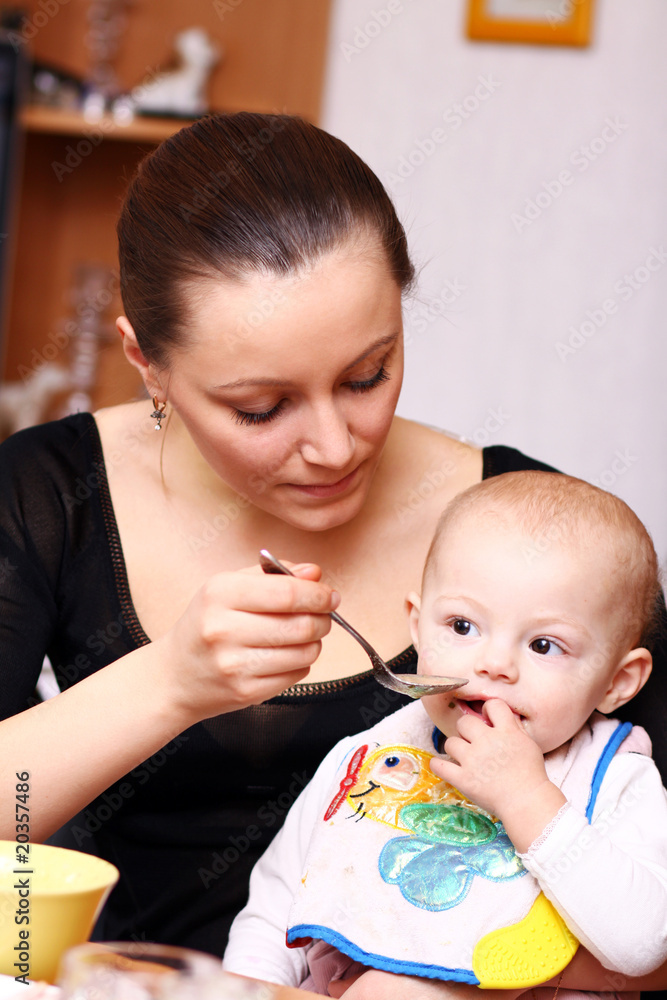 Mum spoon-feeds the child in house interior Mum spoon-feeds the child in house interior