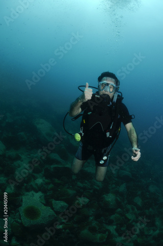young male scuba diver swimming over coral