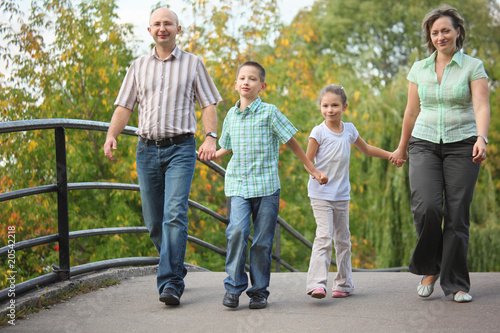 family with two children walking on bridge in early fall park