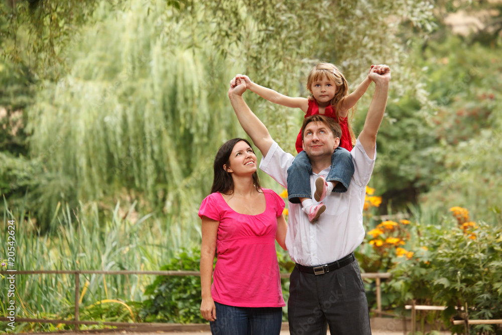 Fototapeta premium Family in summer garden. Girl sits on shoulders at father.