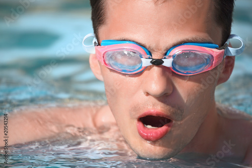 young man in watersport goggles swimming in pool, taking breath