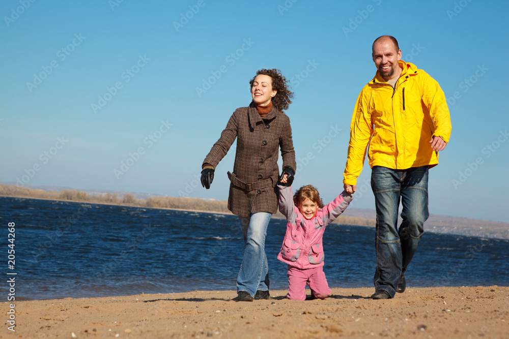 Family of three people walking along beach. Sunny autumn day. Family of three people walking along beach. Sunny autumn day.