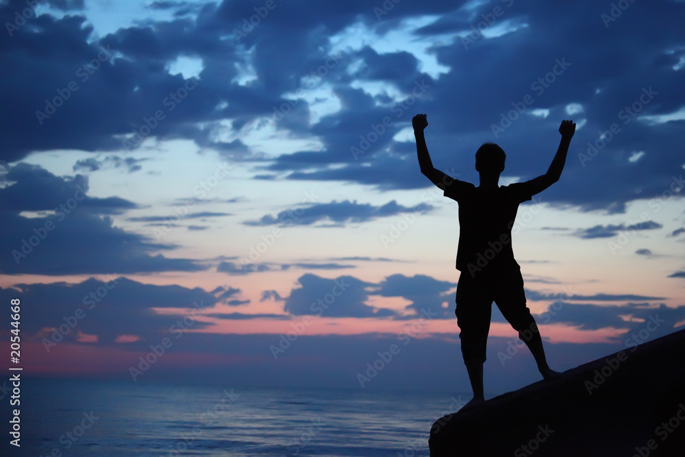 Silhouette guy lifted hands upwards on breakwater in evening