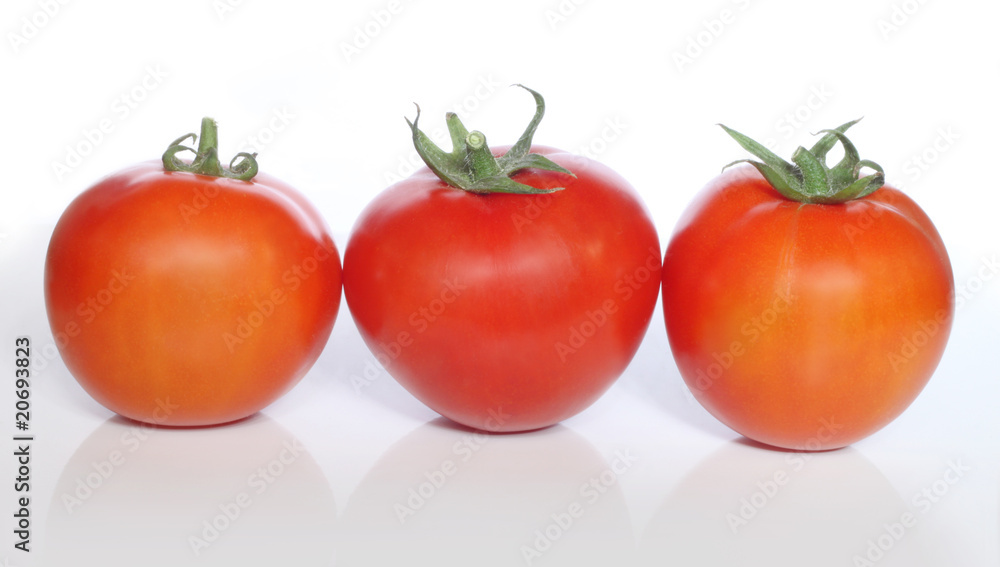 Three tomatoes and their reflection on grayish surface Three tomatoes and their reflection on grayish surface