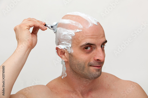Young man shaving his head with razorblade
