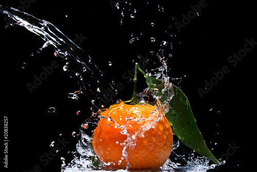 Tangerine with green leaves and water splash isolated on black