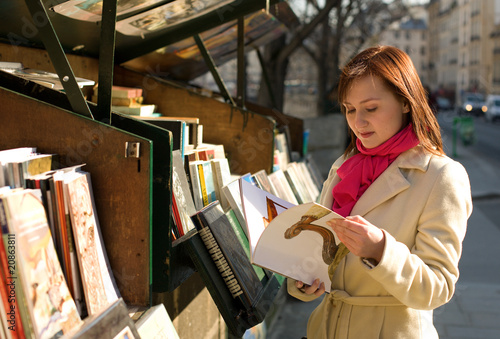 Fotografie Beautiful woman in Paris selecting a book in an outdoor booksel