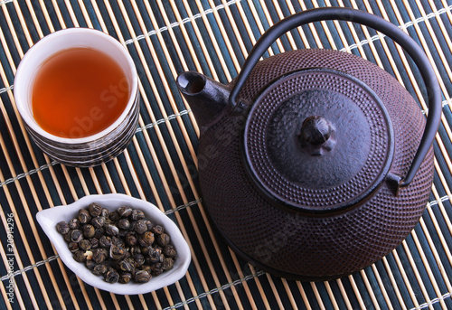 Cast iron TeaPot with teacup and tea leaves on a bamboo mat