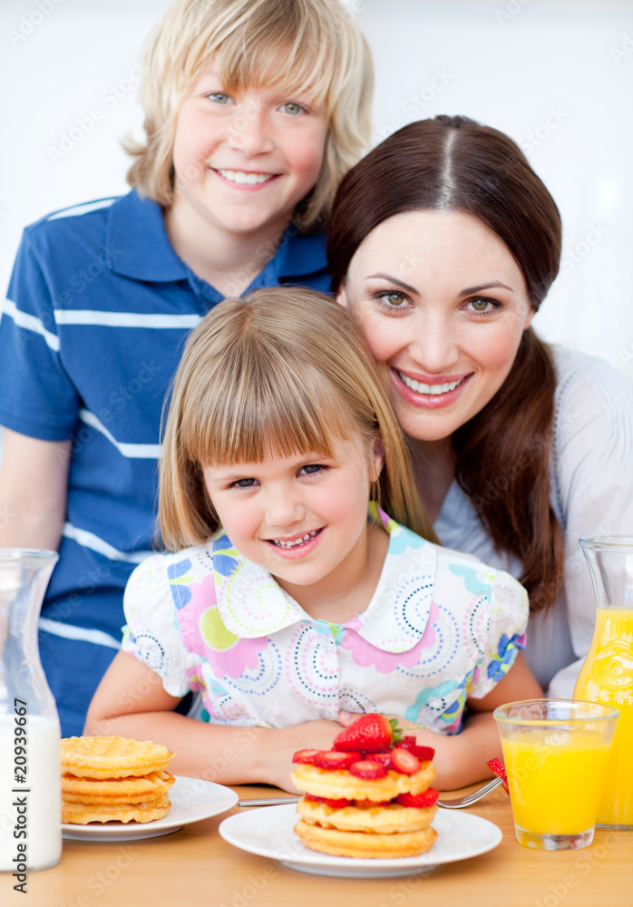 Jolly mother and her children eating waffles with strawberries Jolly mother and her children eating waffles with strawberries