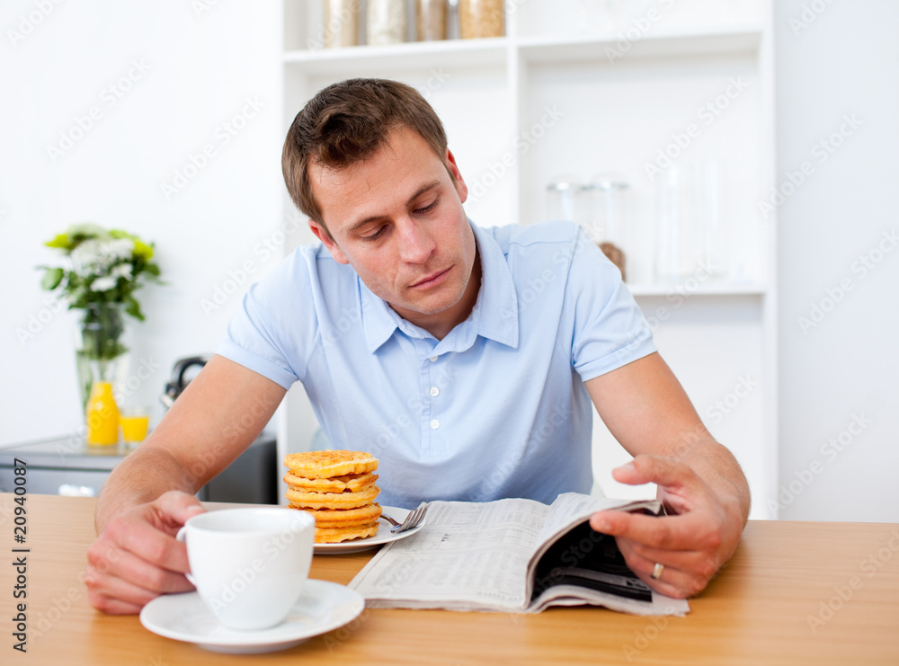 Concentrated man reading a newspaper while having breakfast Concentrated man reading a newspaper while having breakfast
