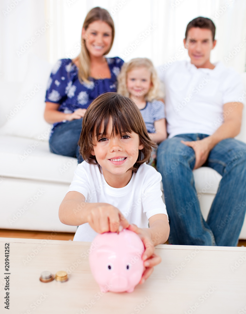 Cheerful little boy inserting coin in a piggybank Cheerful little boy inserting coin in a piggybank