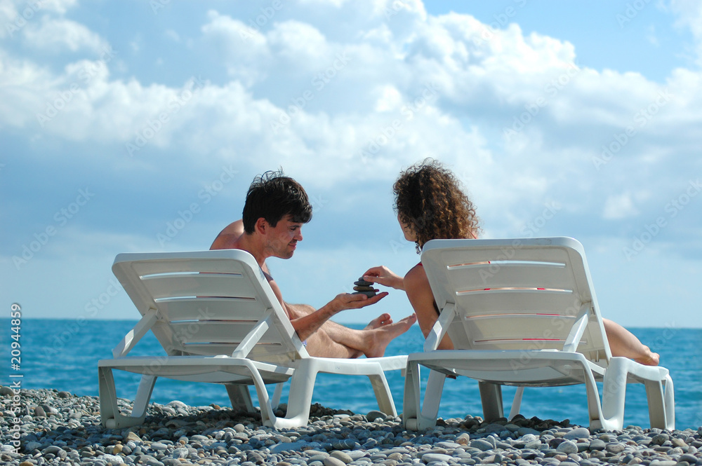 Young man and woman sit in deckchair on beach