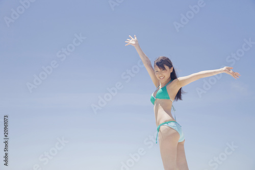青空に両手を挙げる水着女性