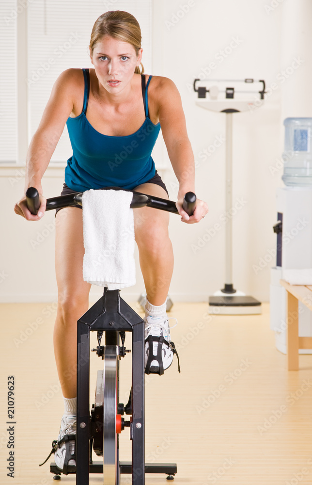 Fototapeta premium Woman riding stationary bicycle in health club