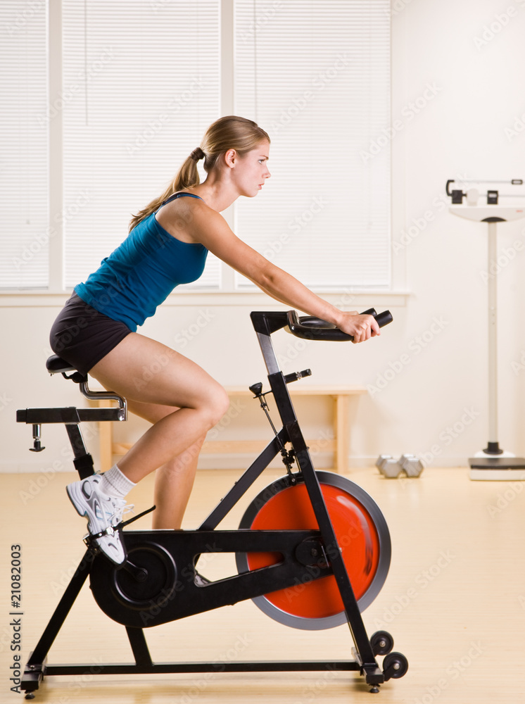Woman riding stationary bicycle in health club Woman riding stationary bicycle in health club