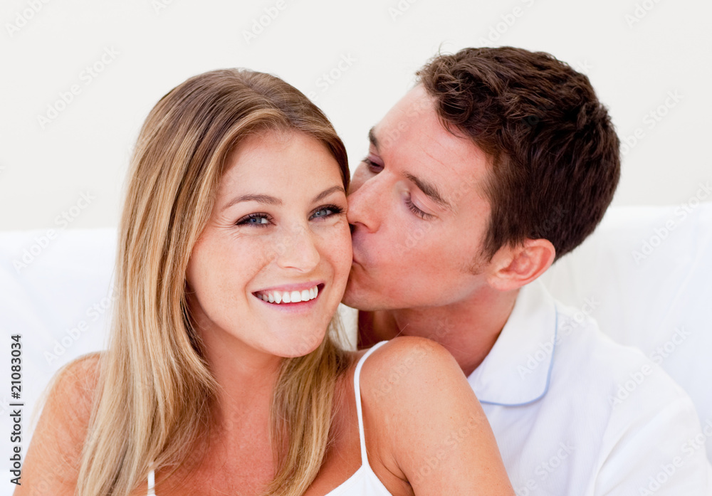 Portrait of an ffectionate man kissing his wife sitting on bed Portrait of an ffectionate man kissing his wife sitting on bed