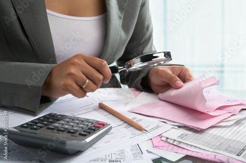 Businesswoman checking bills using magnifying glass photo