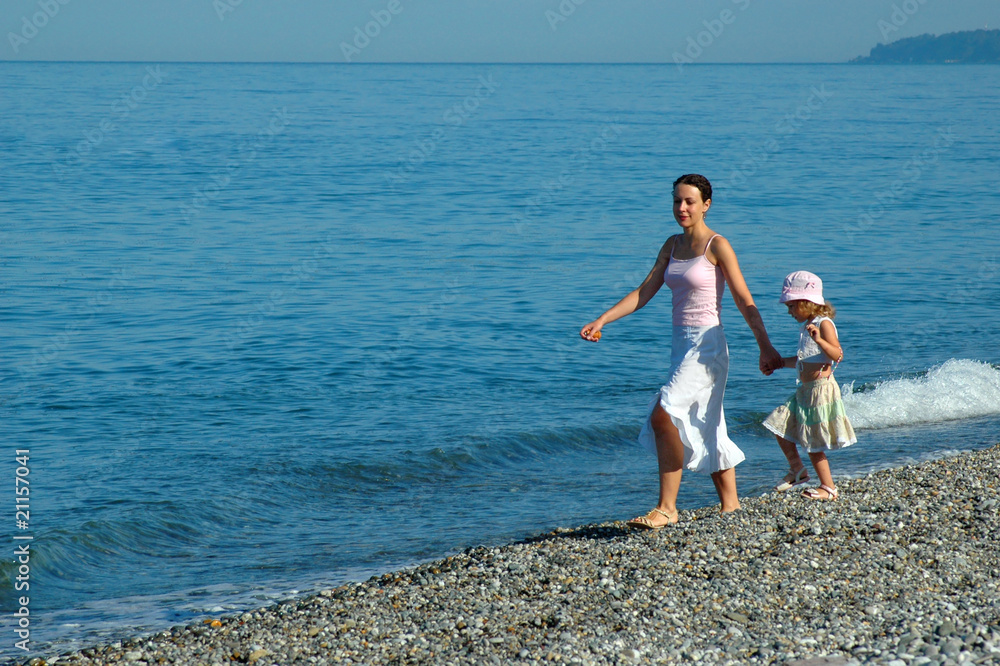 Woman with small girl go on seaside