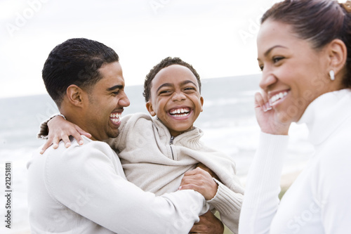 Ten year old African-American boy with parents laughing on beach