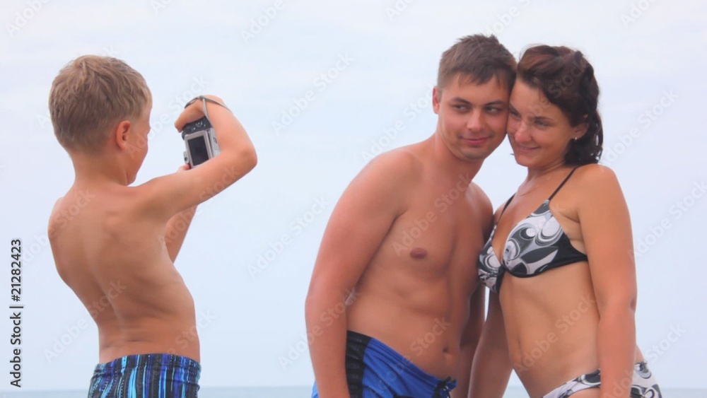 boy photographing man and woman dressed in swimsuit on beach boy photographing man and woman dressed in swimsuit on beach
