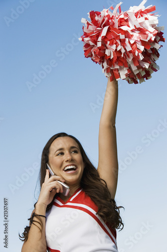 smiling cheerleader rising pom-pom talking on mobile phone (low angle view)
